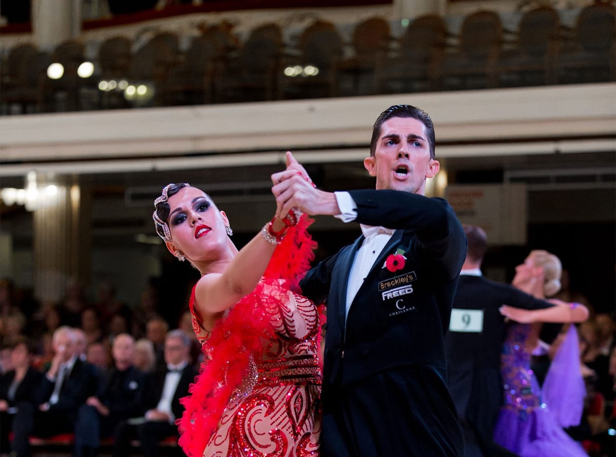 Ballroom couple competing, the woman in a red feathered dress and the man in a tailsuit, spectators behind