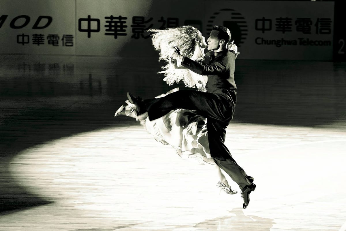 Black-and-white: ballroom couple Mirko Gozzoli and Edita Daniute leaping across a spotlit floor