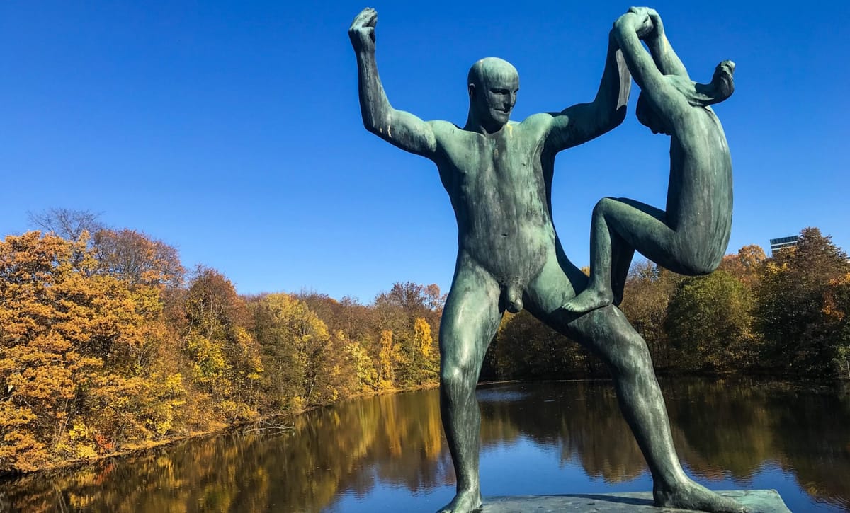 Vigeland bronze of a man holding a figure upside down, above a pond and autumn trees in Oslo