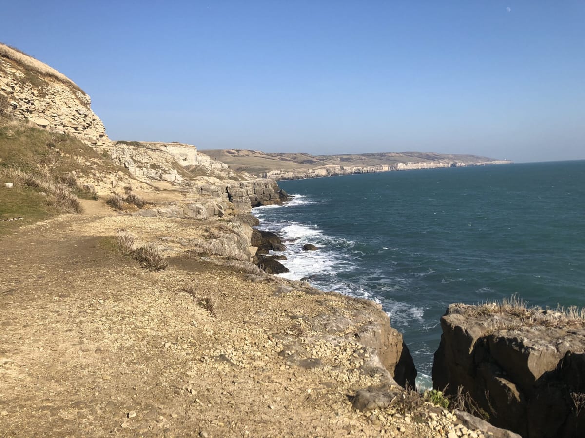 Coast path along pale limestone cliffs above a churning blue sea on a clear day