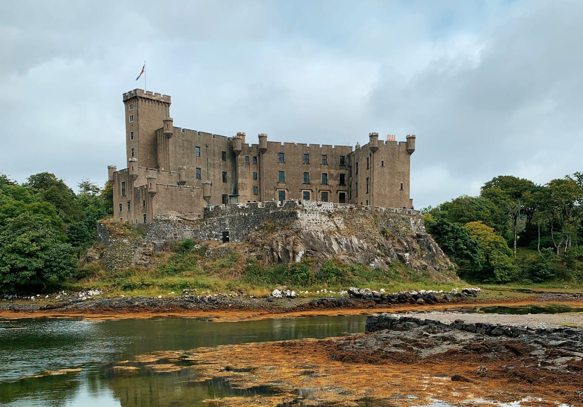 Dunvegan Castle on a rocky outcrop above a seaweed-strewn shore under an overcast sky