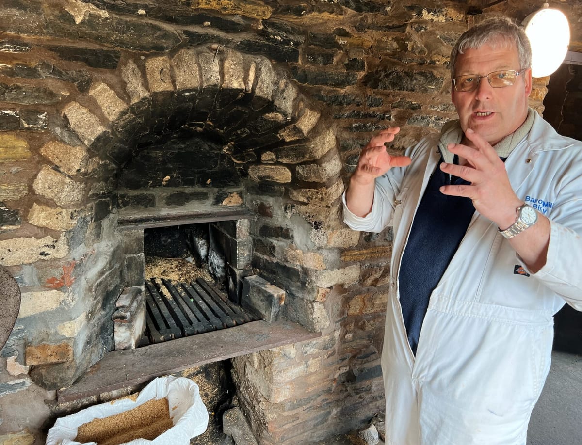 Miller in white overalls gesturing beside a stone kiln at Barony Mill