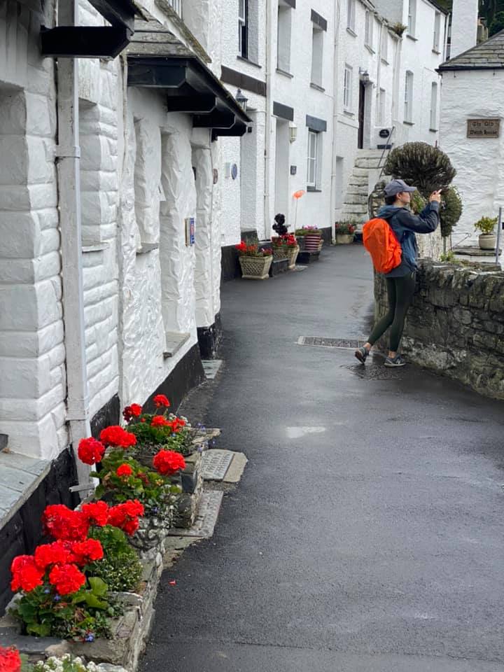 Narrow Polperro lane of white cottages with red geraniums, a visitor taking photos