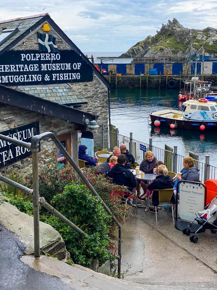People at outdoor tables of the Polperro Heritage Museum of Smuggling & Fishing tea room by the harbour